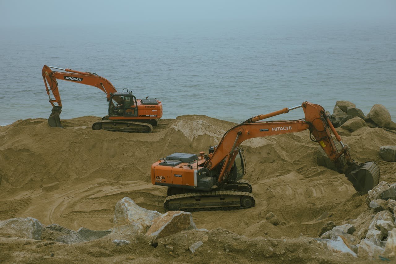 The Art of Drawing Readers In: Your attractive post title goes here Two excavators operate at a sandy construction site by the sea, moving sand and rock.